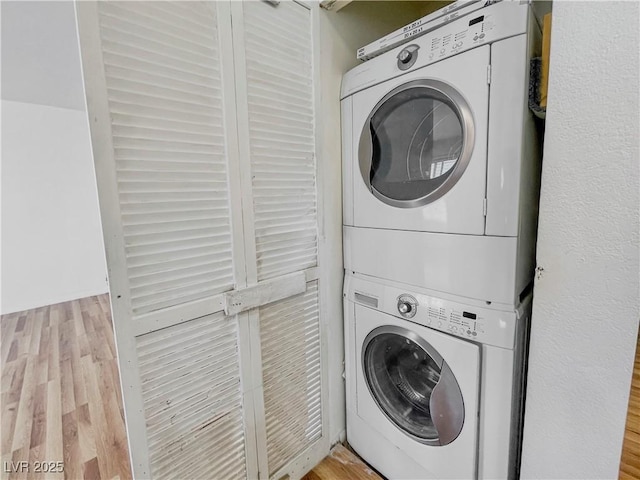 laundry area featuring stacked washer / drying machine, wood finished floors, and laundry area