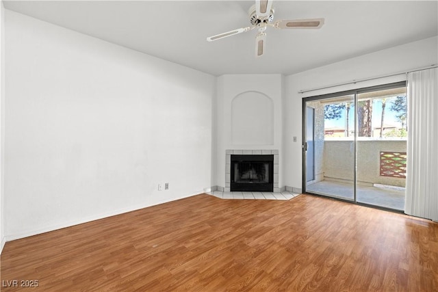unfurnished living room with baseboards, a tiled fireplace, wood finished floors, and ceiling fan