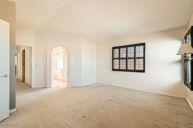 carpeted empty room featuring arched walkways and baseboards