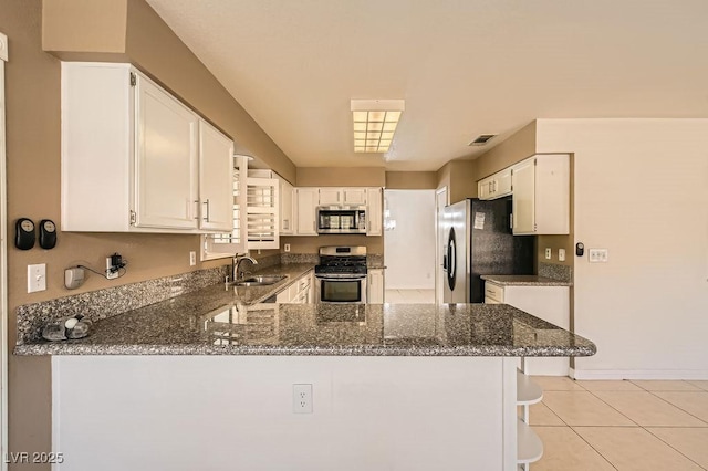 kitchen featuring dark stone countertops, visible vents, a sink, a peninsula, and appliances with stainless steel finishes