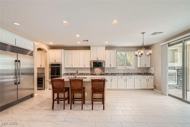 3428 Iron Hagen Ct, Las Vegas, NV 89141 - kitchen with white cabinets, decorative light fixtures, backsplash, appliances with stainless steel finishes, and wine cooler