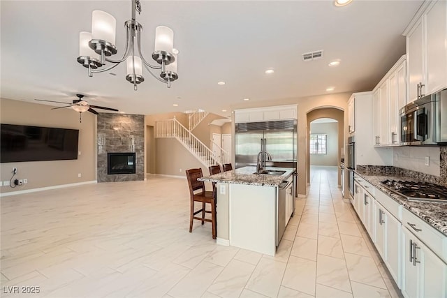 3428 Iron Hagen Ct, Las Vegas, NV 89141 - kitchen with stainless steel appliances, visible vents, arched walkways, a premium fireplace, and ceiling fan with notable chandelier