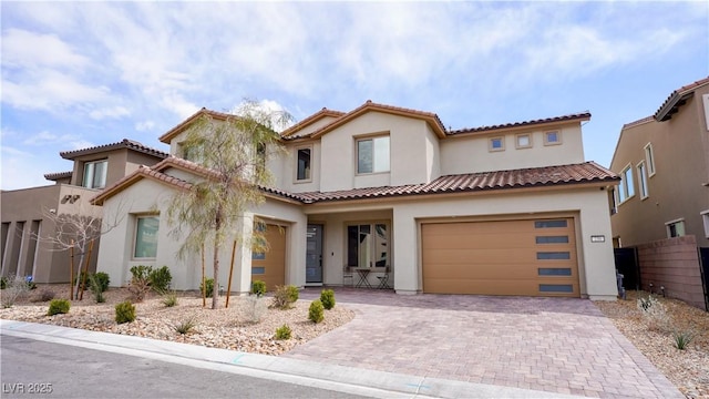 mediterranean / spanish home with stucco siding, decorative driveway, a tiled roof, and a garage