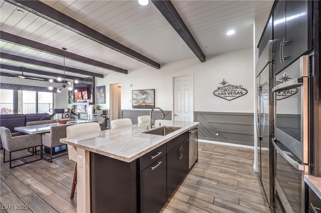kitchen with light wood finished floors, a sink, wainscoting, open floor plan, and a breakfast bar area