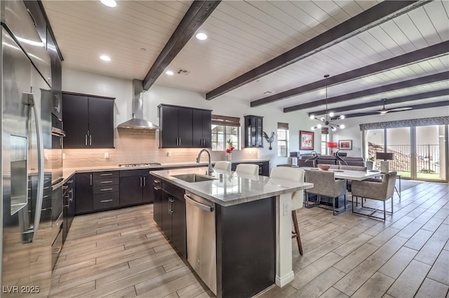 kitchen with light wood-style flooring, a sink, open floor plan, wall chimney range hood, and appliances with stainless steel finishes