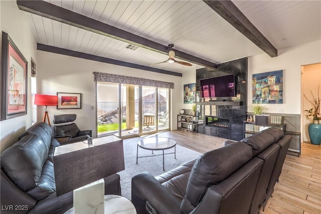 living area featuring beam ceiling, wood finished floors, visible vents, and a premium fireplace