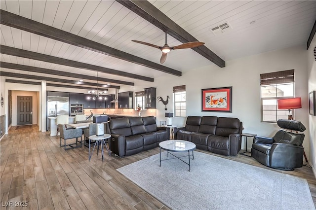 living room with ceiling fan with notable chandelier, wood finished floors, visible vents, and beam ceiling