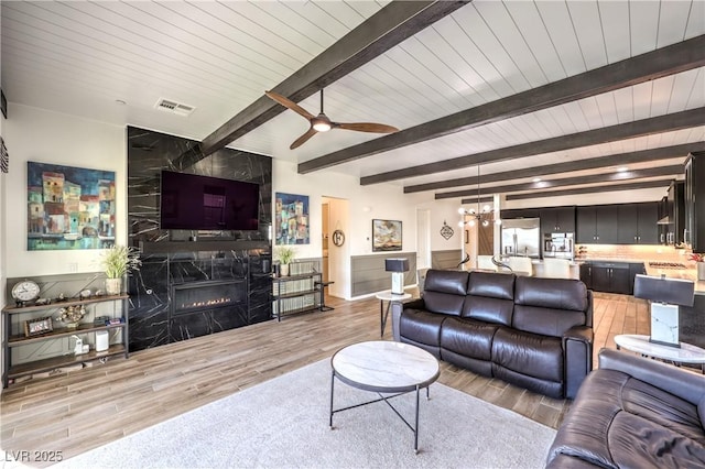 living area featuring beamed ceiling, a premium fireplace, light wood-style floors, and visible vents