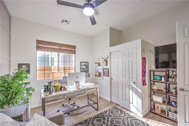 home office with light wood-type flooring, visible vents, a ceiling fan, and baseboards