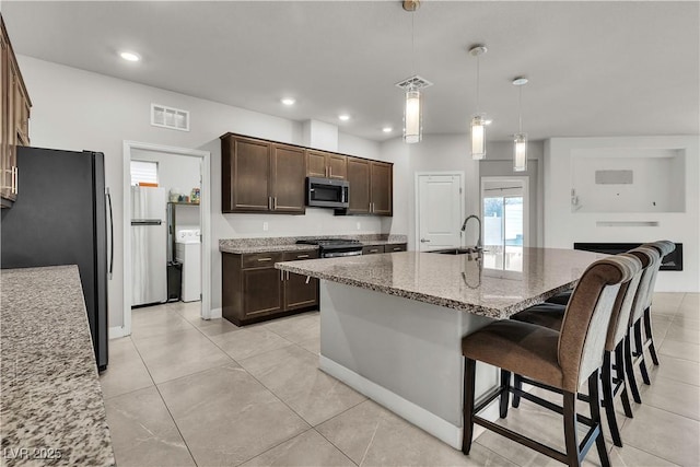 kitchen with dark brown cabinets, a sink, stainless steel appliances, visible vents, and light stone counters