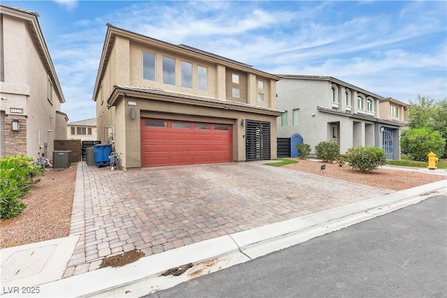 view of front facade featuring central air condition unit, stucco siding, decorative driveway, and a garage