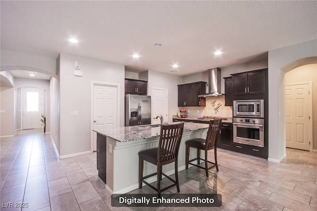 10470 Irish Cliffs Ct, Las Vegas, NV 89149 - kitchen featuring light stone countertops, dark brown cabinetry, stainless steel appliances, a sink, and wall chimney exhaust hood