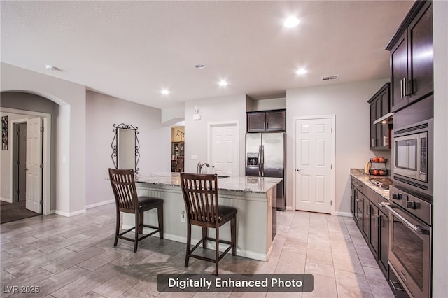 10470 Irish Cliffs Ct, Las Vegas, NV 89149 - kitchen featuring appliances with stainless steel finishes, arched walkways, recessed lighting, light stone countertops, and a kitchen island with sink