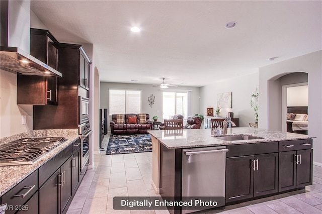 10470 Irish Cliffs Ct, Las Vegas, NV 89149 - kitchen featuring a sink, stainless steel appliances, arched walkways, wall chimney exhaust hood, and a kitchen island with sink