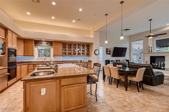 kitchen featuring light stone countertops, a center island with sink, light tile patterned flooring, and a sink