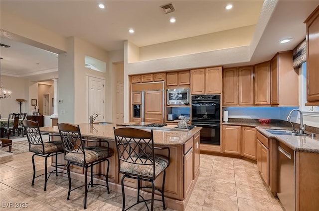 kitchen featuring light stone countertops, an island with sink, a breakfast bar, built in appliances, and a sink