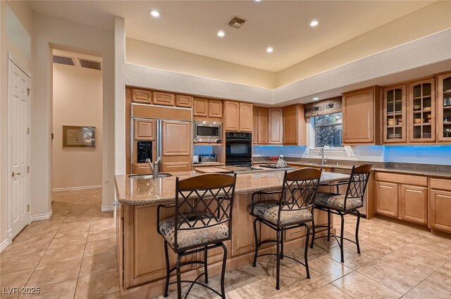 kitchen featuring glass insert cabinets, a breakfast bar, a kitchen island, built in appliances, and a sink