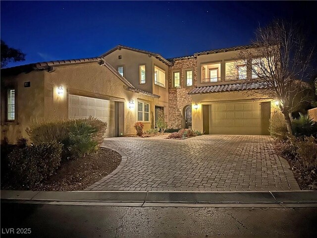mediterranean / spanish home featuring stucco siding, stone siding, a tiled roof, and decorative driveway