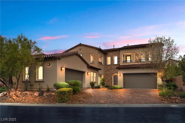 mediterranean / spanish house featuring stone siding, a tiled roof, stucco siding, and decorative driveway