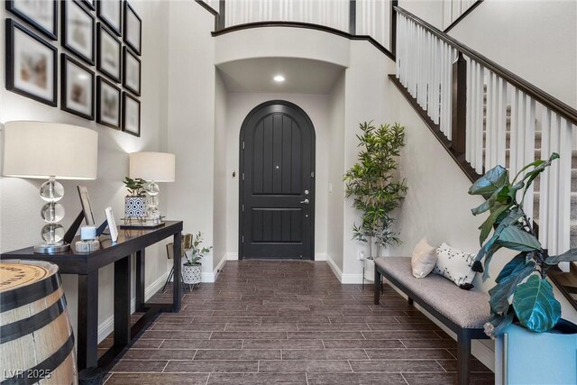 entryway featuring wood tiled floor, a high ceiling, arched walkways, baseboards, and stairs
