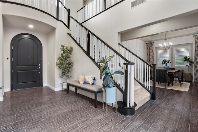 foyer entrance featuring stairway, wood finished floors, a chandelier, baseboards, and visible vents
