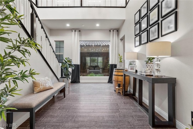 corridor featuring baseboards, recessed lighting, wood finished floors, a high ceiling, and stairway
