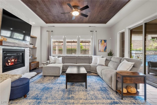 living area with a tray ceiling, visible vents, wooden ceiling, and ceiling fan