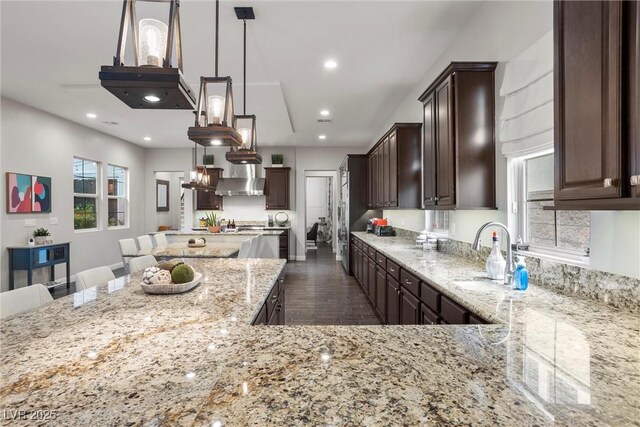 kitchen with a center island, a sink, dark brown cabinets, recessed lighting, and light stone countertops