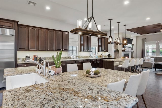 kitchen with dark brown cabinets, visible vents, a sink, stainless steel built in fridge, and a center island