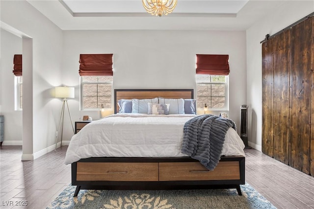 bedroom featuring a barn door, baseboards, wood finished floors, and a raised ceiling