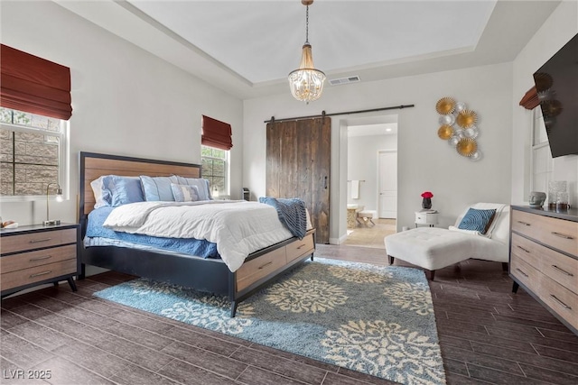 bedroom with a barn door, a raised ceiling, wood finished floors, and visible vents
