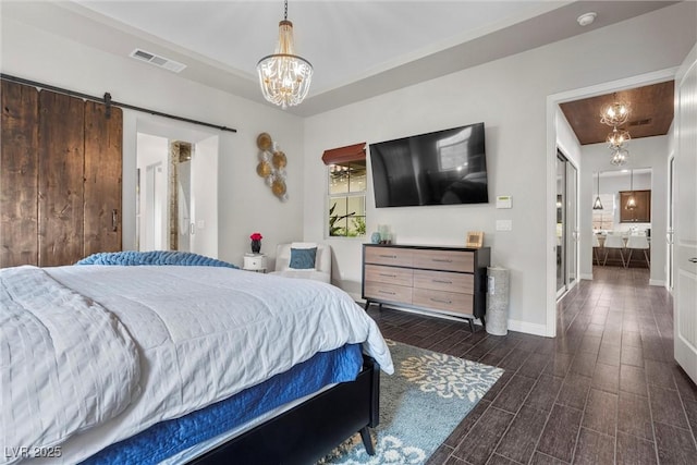 bedroom with a barn door, a chandelier, baseboards, wood finish floors, and visible vents