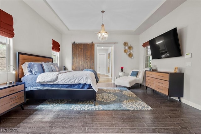 bedroom with a barn door, wood tiled floor, a raised ceiling, and multiple windows