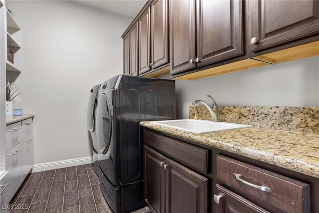 washroom with a sink, wood finish floors, washer and dryer, cabinet space, and baseboards