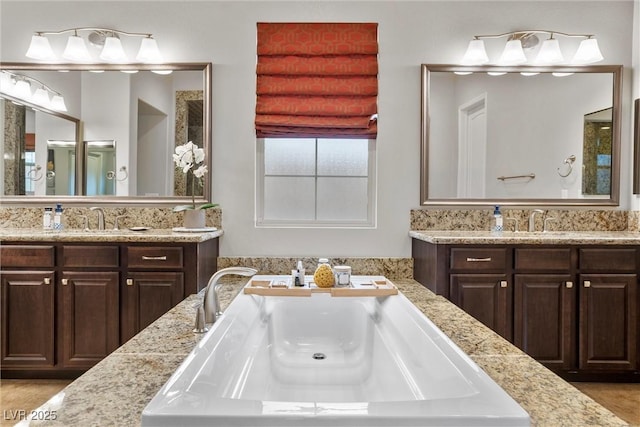 full bathroom featuring two vanities, a tub with jets, and a sink