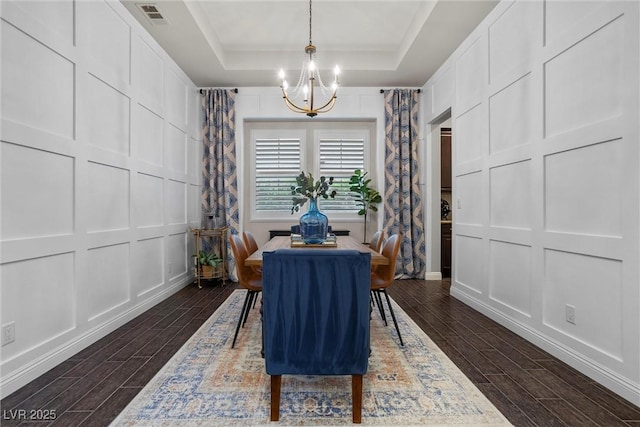 dining room featuring dark wood-type flooring, a decorative wall, a notable chandelier, and visible vents