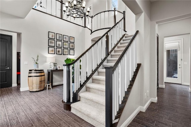 staircase featuring wood finished floors, a towering ceiling, baseboards, and an inviting chandelier