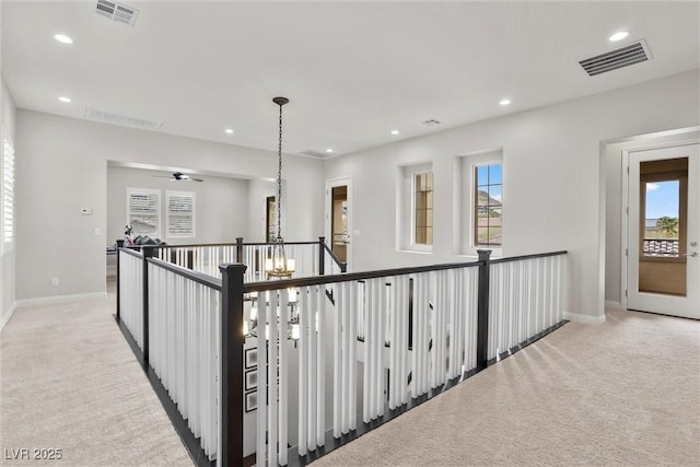 corridor featuring baseboards, visible vents, and light colored carpet