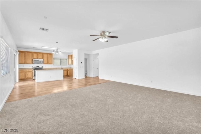 5060 Blue Rose St, North Las Vegas, NV 89081 - unfurnished living room featuring visible vents, light carpet, light wood-type flooring, baseboards, and ceiling fan with notable chandelier