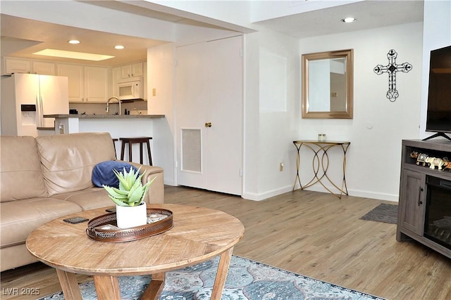 living room featuring baseboards, visible vents, light wood finished floors, and recessed lighting