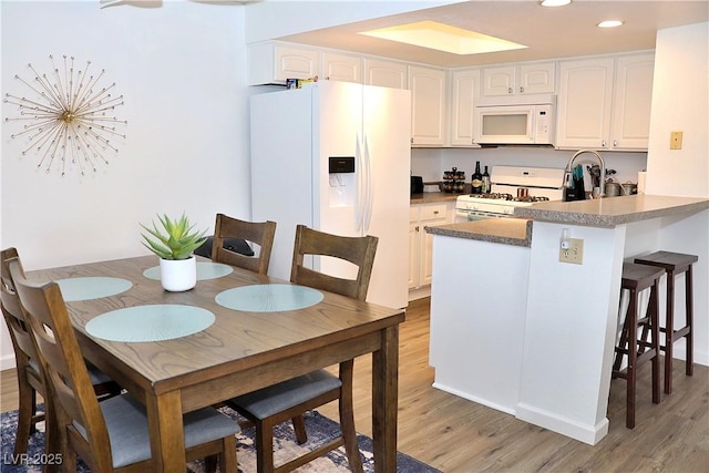 kitchen featuring a peninsula, white cabinetry, white appliances, and light wood-style flooring