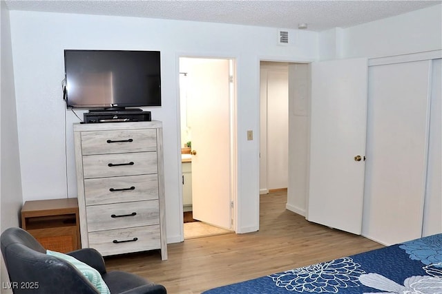 bedroom with connected bathroom, a textured ceiling, visible vents, and light wood-style flooring