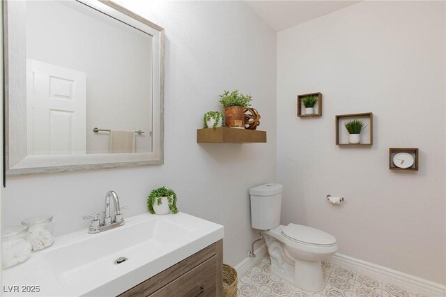 half bathroom featuring vanity, toilet, baseboards, and tile patterned floors
