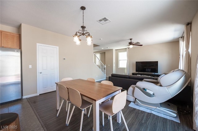 dining area featuring stairway, dark tile patterned flooring, ceiling fan with notable chandelier, baseboards, and visible vents