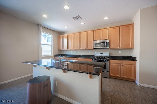kitchen featuring stainless steel appliances, dark countertops, visible vents, a sink, and a breakfast bar area