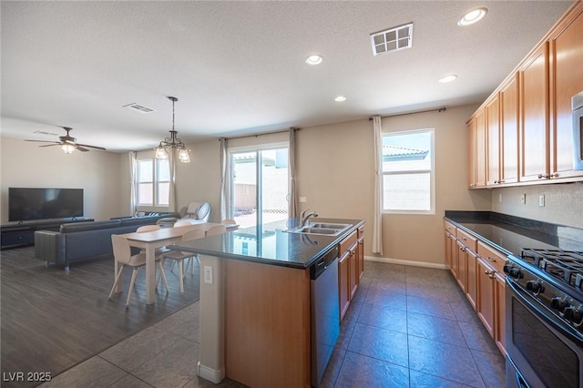kitchen with dishwasher, dark countertops, a sink, and visible vents