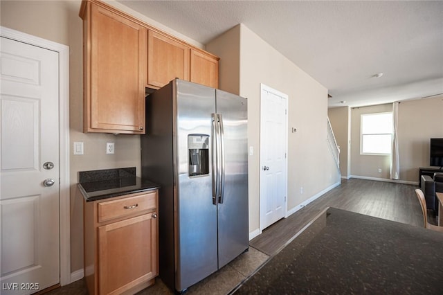 kitchen with open floor plan, baseboards, dark stone countertops, and stainless steel fridge with ice dispenser