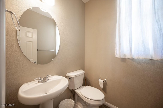 bathroom featuring a textured wall, toilet, and a sink