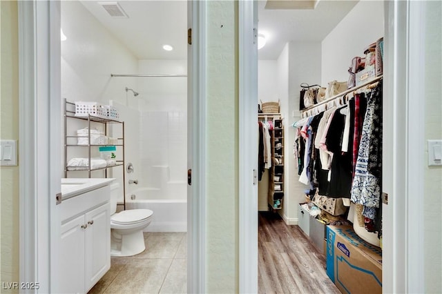 full bathroom with visible vents, toilet, vanity, a walk in closet, and tub / shower combination