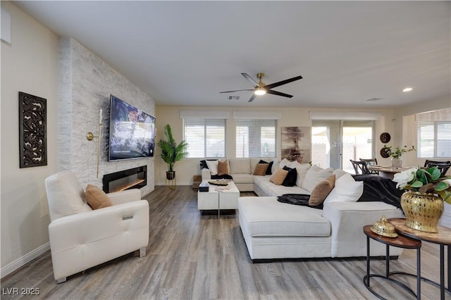 living room with wood finished floors, visible vents, baseboards, a fireplace, and ceiling fan
